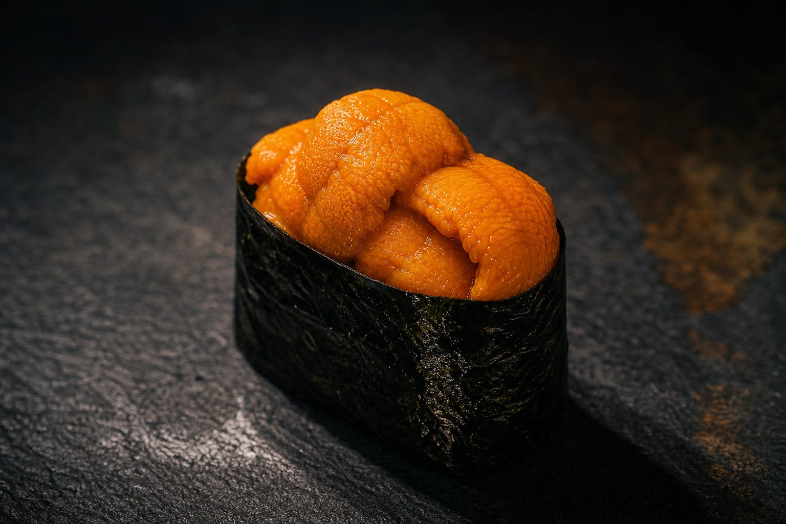 A gunkan of vivid orange Hokkaido sea urchin wrapped in dark nori on slate